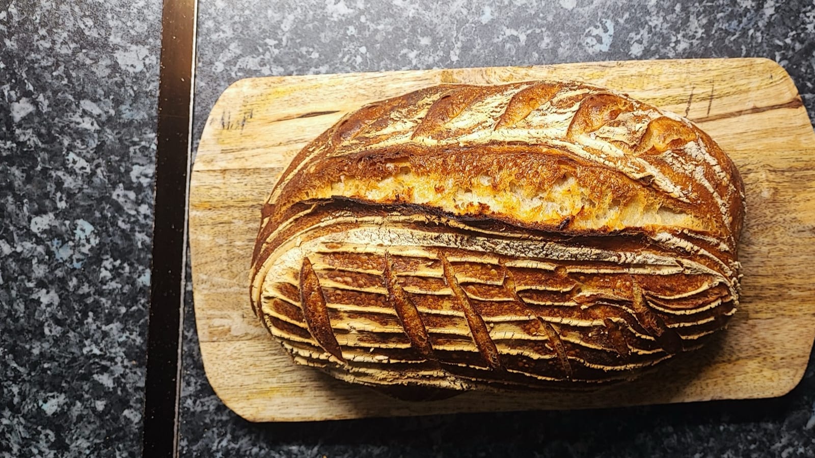 Finished sourdough loaf with decorative scoring on a wooden board